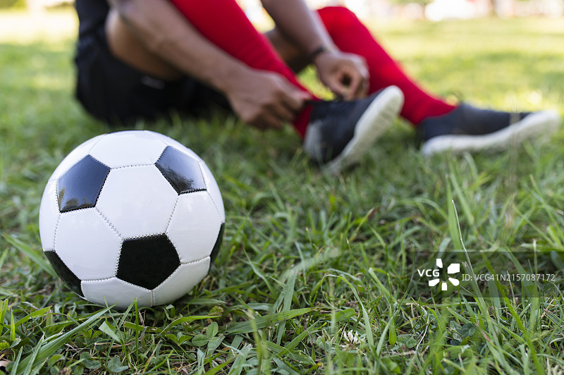 草地上白色足球，背景是系鞋带的球员图片素材
