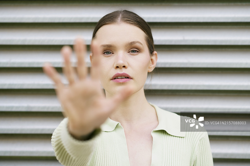 微笑的女人在墙边面无表情地做出停止手势图片素材