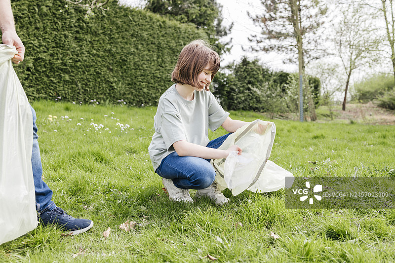 在草地上和父亲一起用袋子收集塑料垃圾的微笑女孩图片素材
