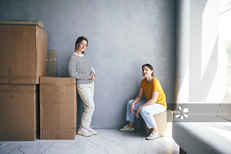 两位女人在堆叠的纸板箱旁休息，搬家期间小憩图片素材