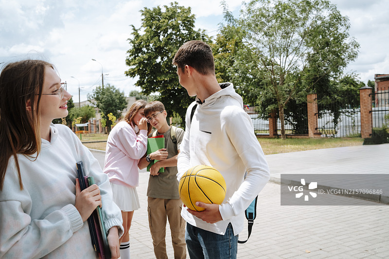 阳光明媚的校园里，少女在朋友旁向男孩耳语图片素材