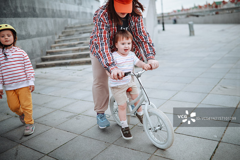 兄弟姐妹关怀:少女帮助蹒跚学步的弟弟骑平衡车，家人的爱图片素材