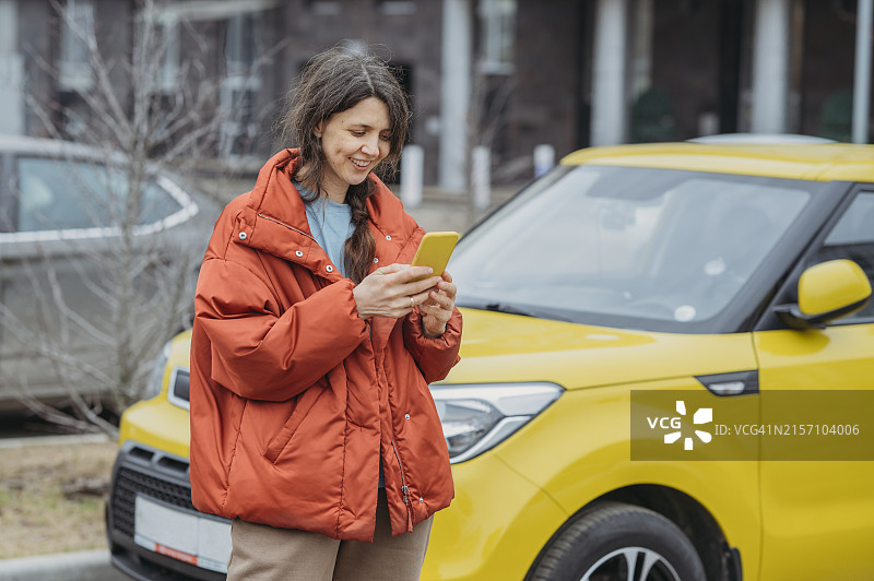 微笑的女人在街上站在黄色汽车旁使用智能手机图片素材