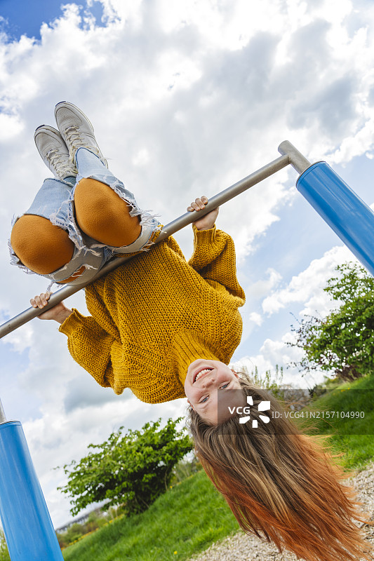 在多云天空下，快乐的女孩在体操杆上倒挂图片素材