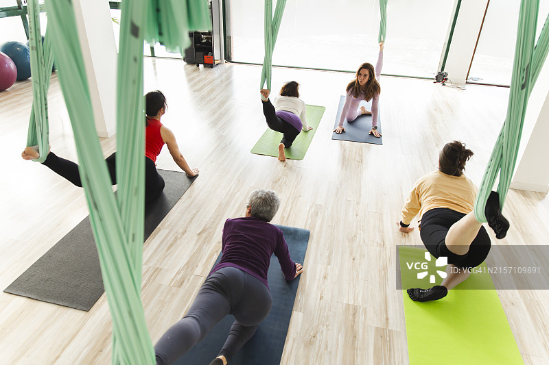 瑜伽教练与女性在课堂上用空中绸缎和垫子练习伸展运动图片素材