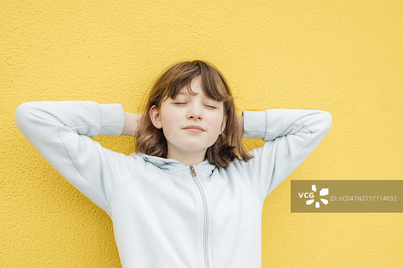 闭着眼睛，靠在黄色墙壁上的女孩图片素材