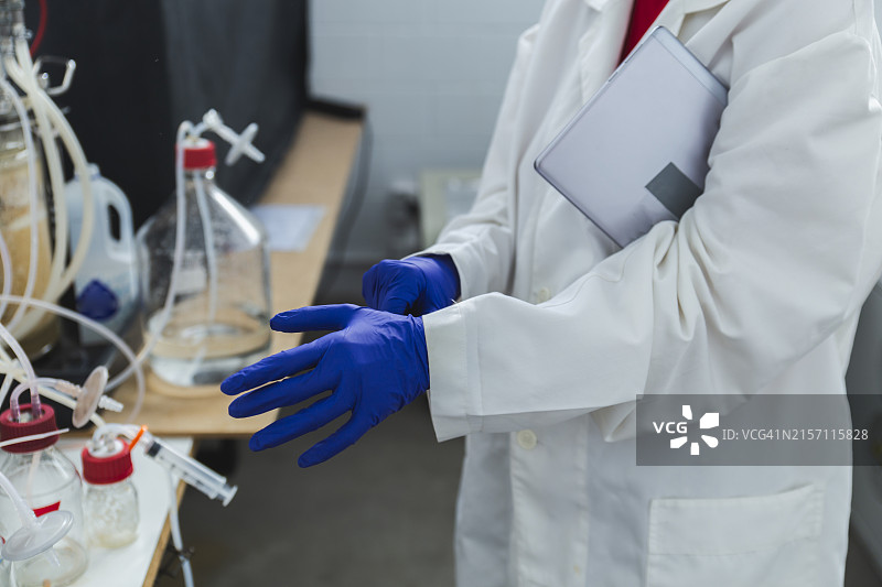 在实验室站在生物反应器旁的戴手套的科研人员图片素材