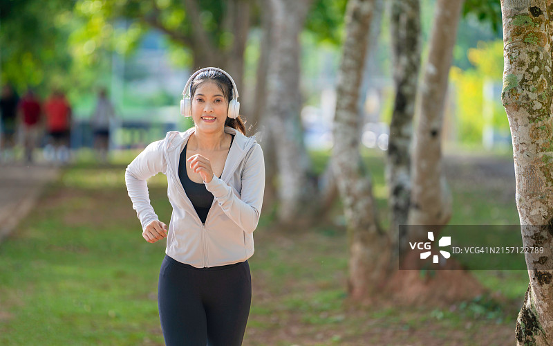 年轻的健身运动女性在公园跑步，戴着耳机在户外晨跑图片素材