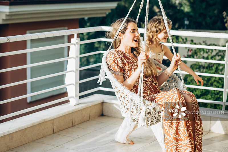 阳光明媚的日子里，母女在户外一起荡秋千，享受欢乐时光。图片素材