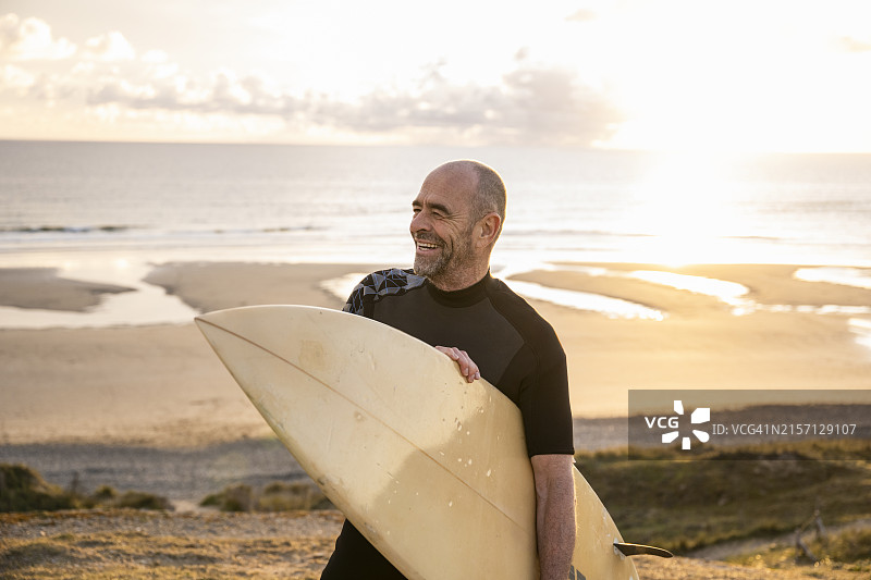 微笑的中年男子在海滩上扛着冲浪板图片素材