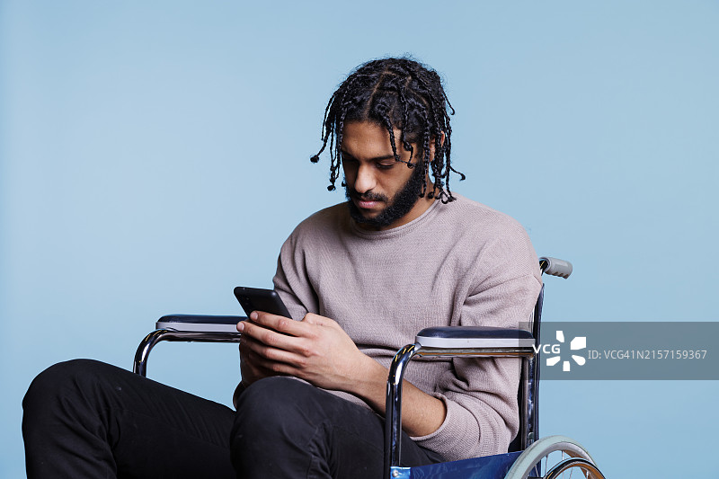 坐在轮椅上的男子在智能手机上浏览社交媒体图片素材