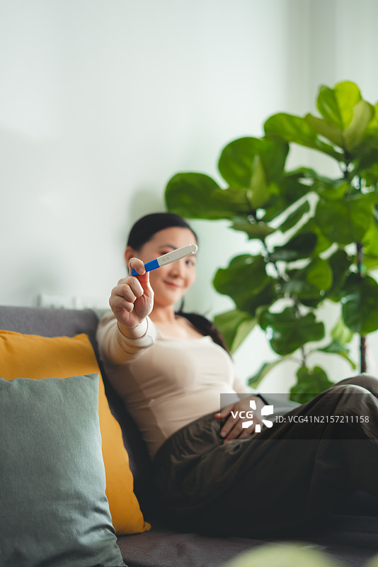 亚洲女人手持验孕棒，坐在沙发上高兴地看着镜头图片素材