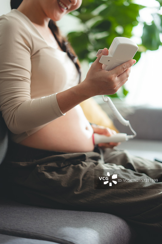 孕妇在家坐在沙发上，用胎心仪听宝宝心跳的特写图片素材