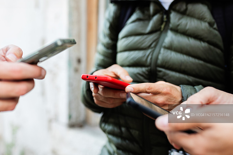 三位身份不明的人在城市街道上一起使用手机的特写镜头图片素材
