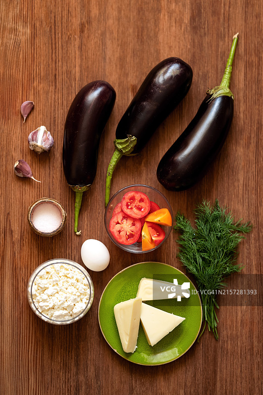 木桌上的茄子。菜的配料。早餐。蔬菜配奶酪、香草和鸡蛋。切片奶酪，西红柿。一束莳萝。仍然生活。前视图。木制背景。图片素材