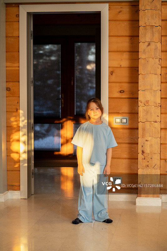穿着蓝色家居服的女孩站在家中夕阳的余晖里图片素材
