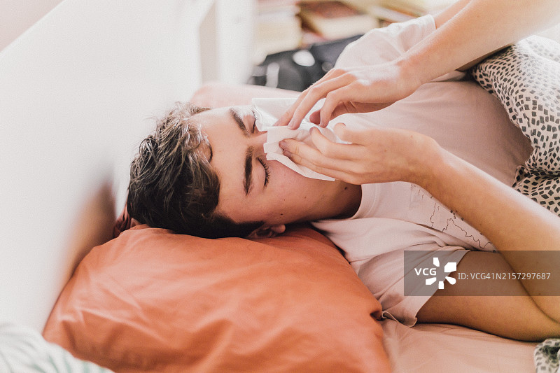 男青少年在床上用纸巾擦鼻涕图片素材