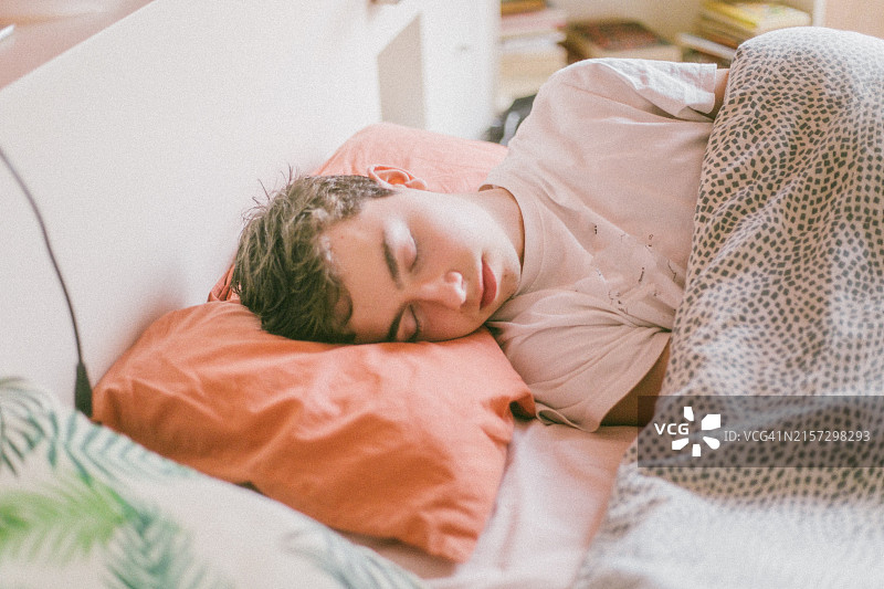 一个年轻人在卧室里睡觉，盖着羽绒被，枕着枕头，非常舒适图片素材