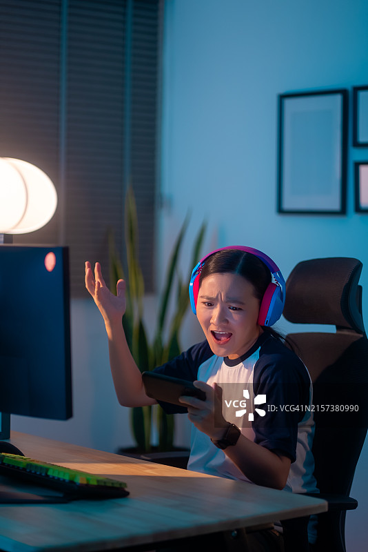 亚洲女性游戏玩家戴着耳机在智能手机上玩游戏，输了后感到沮丧图片素材