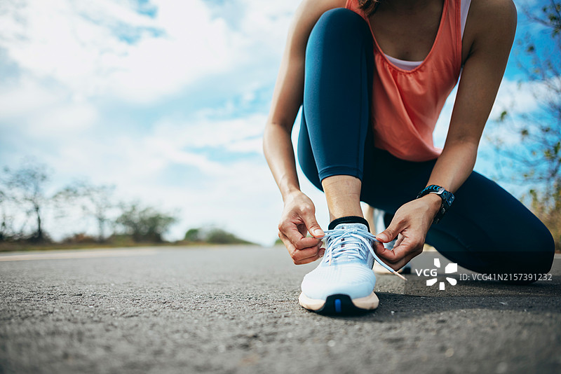 清晨，年轻女子在户外准备慢跑，弯腰系鞋带，确保跑鞋牢固图片素材