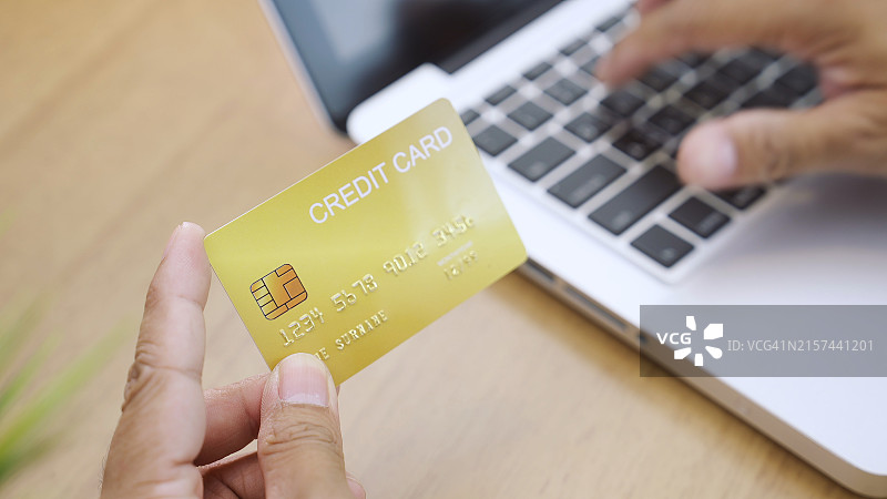 手持信用卡靠近笔记本电脑键盘图片素材