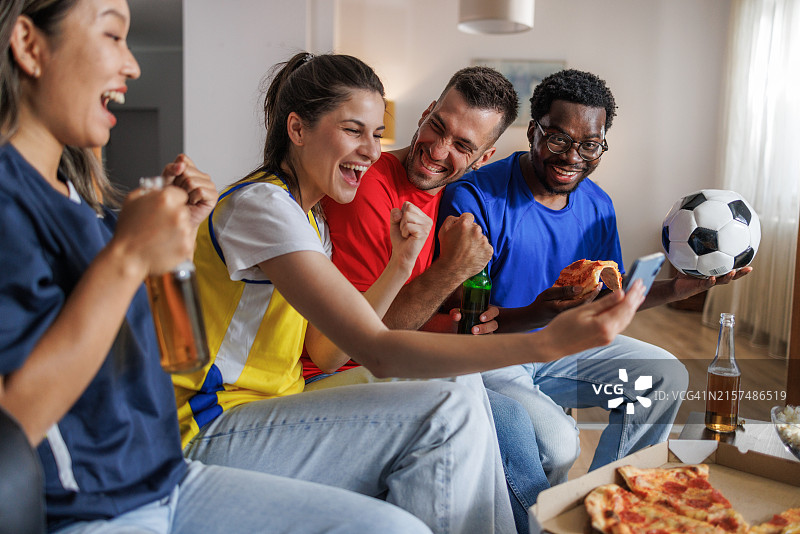 一群朋友在沙发上分享零食和饮料，用智能手机观看足球比赛图片素材