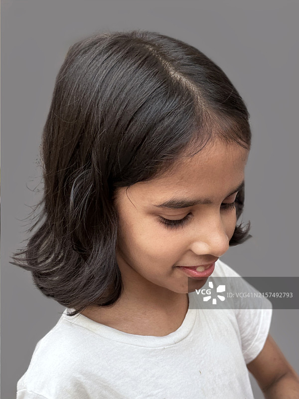 穿着休闲白色T恤的年轻印度女孩，留着波波头，住宅楼灰色背景，侧面轮廓，前景聚焦图片素材