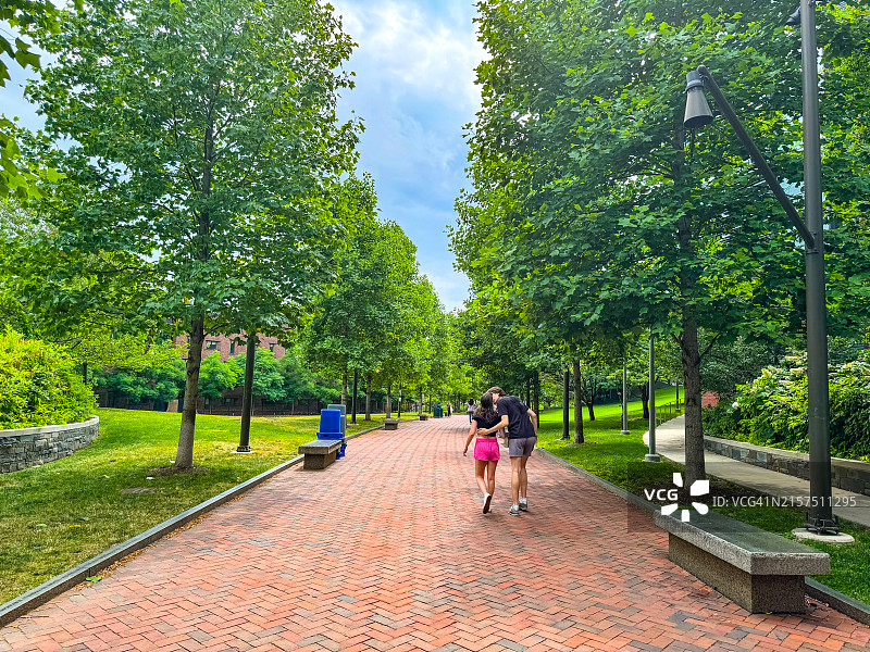 情侣在费城宾夕法尼亚大学校园的树下砖路上拥抱（背面视角）图片素材