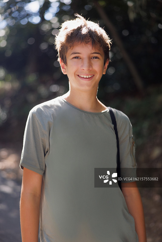 在公园绿荫下享受夏日并对着镜头微笑的漂亮青少年男孩图片素材