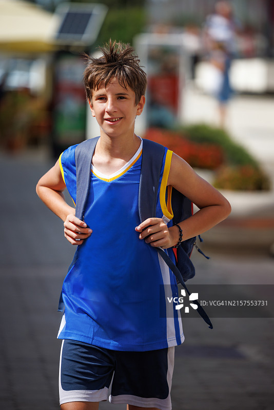 穿着篮球服、背着书包走在夏日街头的青少年男孩图片素材