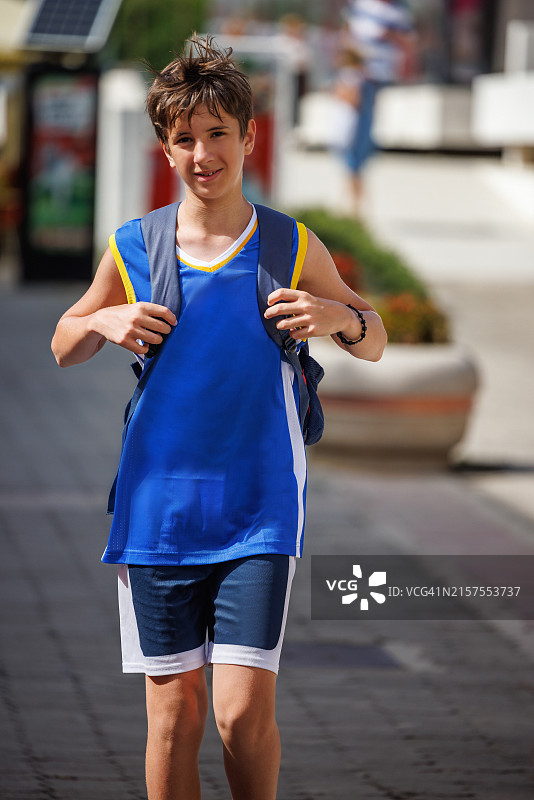 穿着篮球服的青少年男孩在夏天背着背包走在街上图片素材