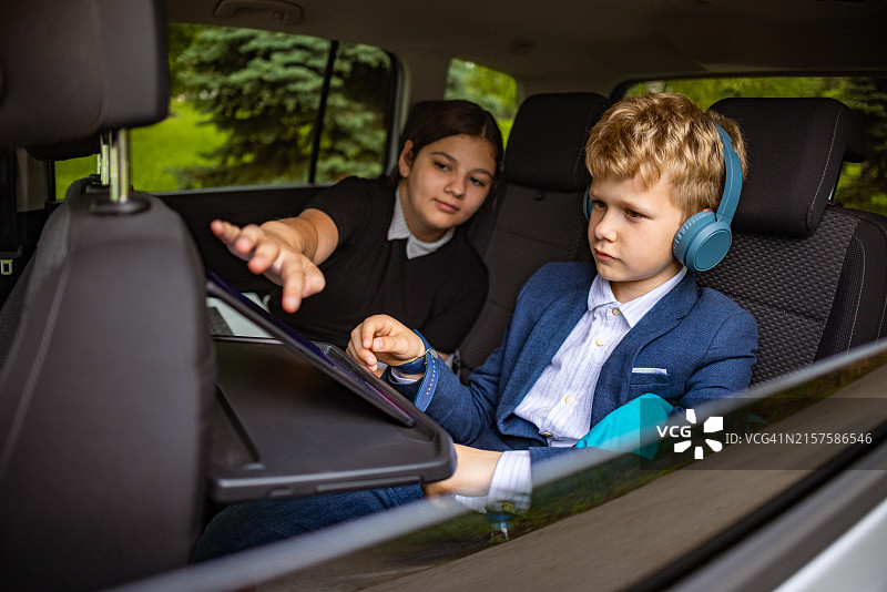 在汽车后座上使用平板电脑和笔记本电脑的白人兄妹图片素材