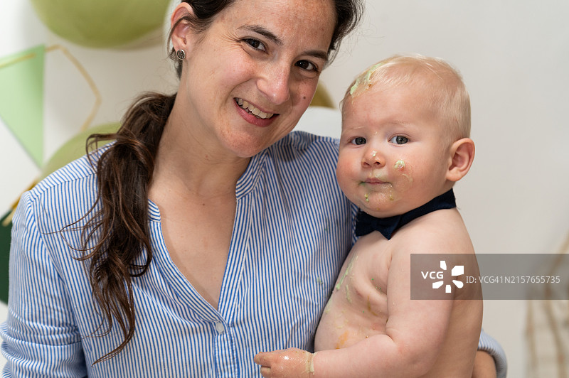 母亲抱着满身蛋糕的一岁男婴图片素材