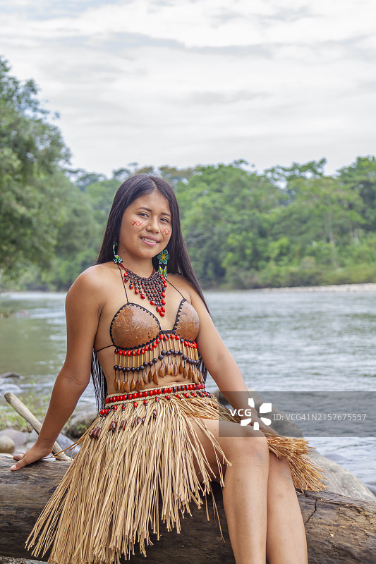 一位年轻美丽的土著女性肖像，穿着部落的传统服装，在村庄里拍摄，背景是亚马逊河。基奇瓦部落。图片素材
