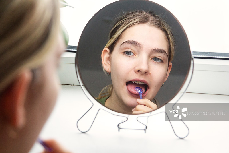 年轻少女在镜子前用刮舌器清洁舌头图片素材