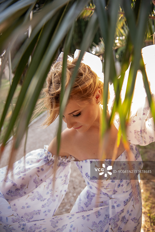 棕榈叶下的碎花裙金发女人图片素材
