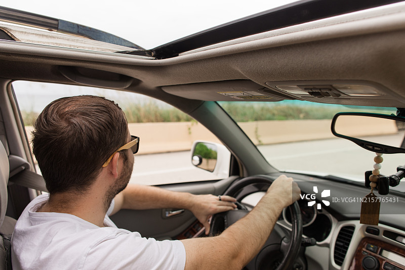 一位33岁的美国男人戴着白色T恤和太阳镜，在佛罗里达州棕榈滩热带度假期间在海边开车并眺望大海图片素材