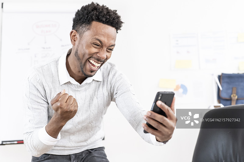 在办公室里举起拳头用手机庆祝的成功商人图片素材