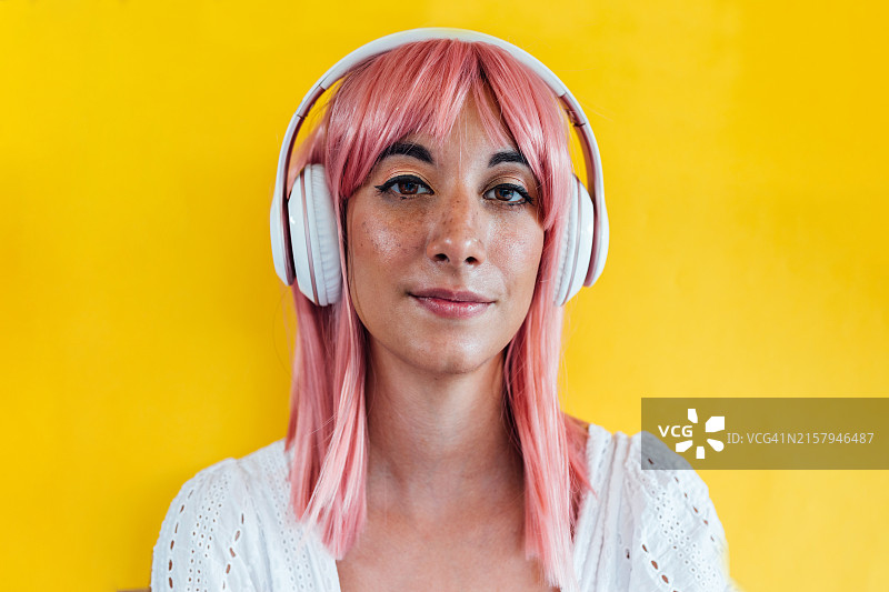 戴耳机粉色头发的忧郁女人在黄色背景上听悲伤的音乐图片素材