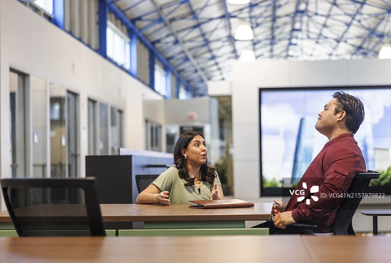 招聘流程:一名西班牙裔女性在一家高科技办公室与一名亚洲男人交谈并进行面试。图片素材