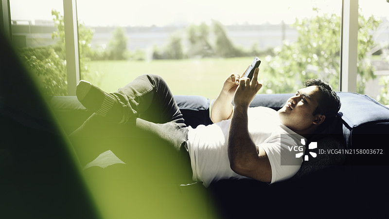 年轻的越南男子在客厅的沙发上放松地使用手机图片素材