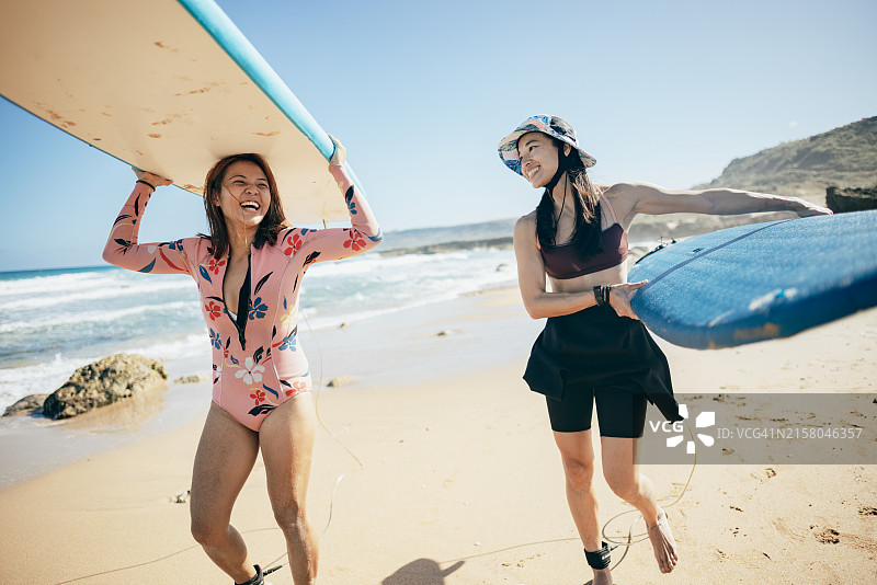 两名兴奋的亚洲女孩拿着冲浪板走在海滩上，准备冲浪图片素材