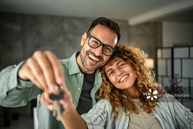 新的开始——一对快乐的夫妇拿着新房的钥匙看着镜头图片素材