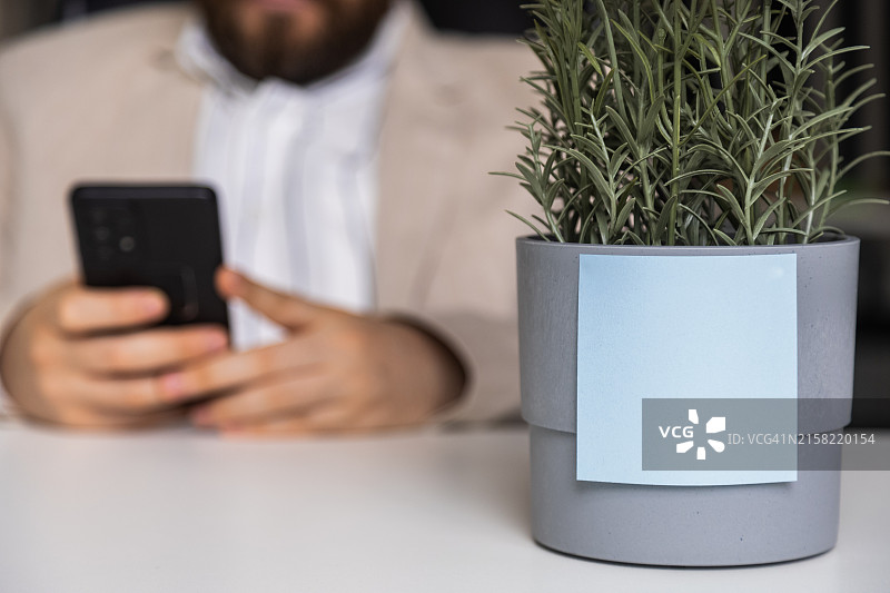 拿着智能手机的商务男人。花盆上带有空白区域的蓝色贴纸便笺图片素材