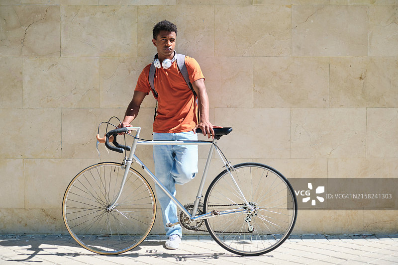 穿着橙色衬衫的学生站在自行车旁图片素材