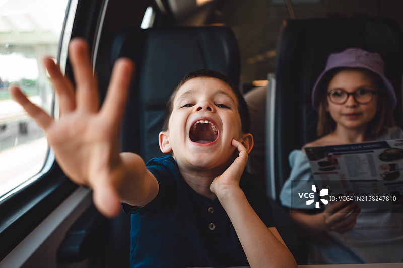 张着嘴的可爱男孩向镜头伸出手，他想要什么。他的妹妹坐在他旁边。他们在火车上图片素材