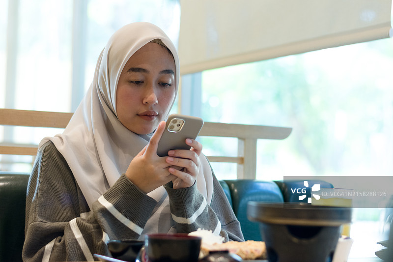 戴头巾的年轻女人在餐厅拍摄美食图片素材
