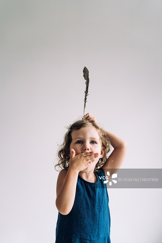 坐在柳条椅上，拿着羽毛假扮印第安人的金发卷发小女孩图片素材