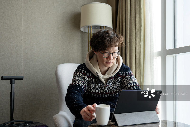 亚洲男子在酒店房间喝咖啡并使用触摸板图片素材