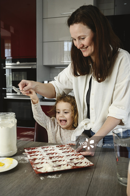 快乐的母女在红色硅胶饼干模具上放面粉图片素材